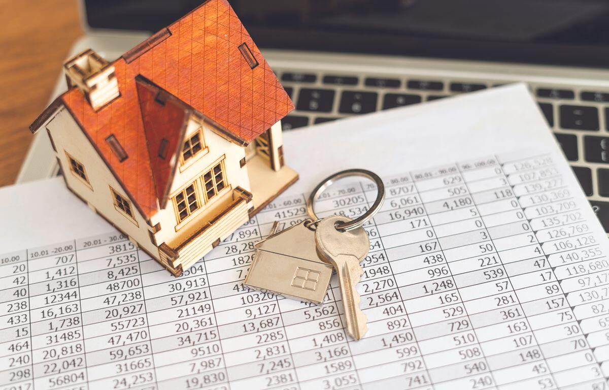 Wooden house model with a key on a financial spreadsheet, symbolizing mortgage or real estate.