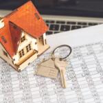 Wooden house model with a key on a financial spreadsheet, symbolizing mortgage or real estate.
