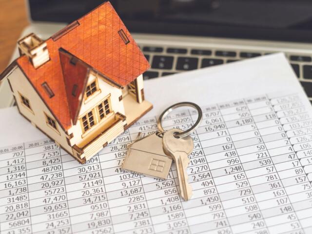 Wooden house model with a key on a financial spreadsheet, symbolizing mortgage or real estate.