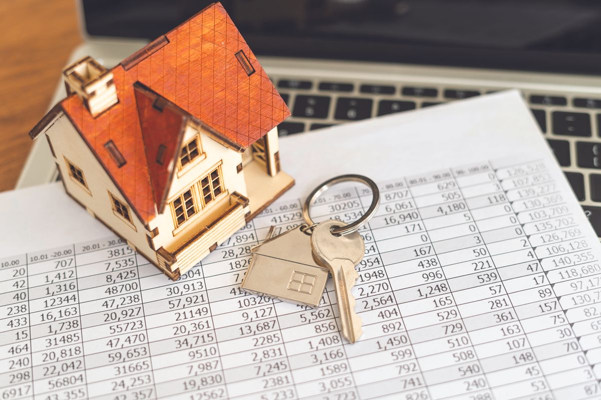 Wooden house model with a key on a financial spreadsheet, symbolizing mortgage or real estate.